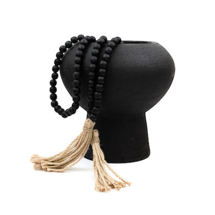 Modern form black vase shown draped with wooden beads